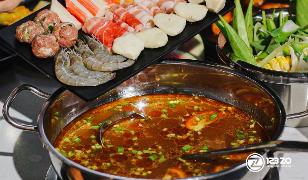Nồi lẩu đậm đà tại HBBQ Buffet, với các món nhúng như thịt bò cuộn, tôm, viên thả lẩu được bày trên đĩa đen.