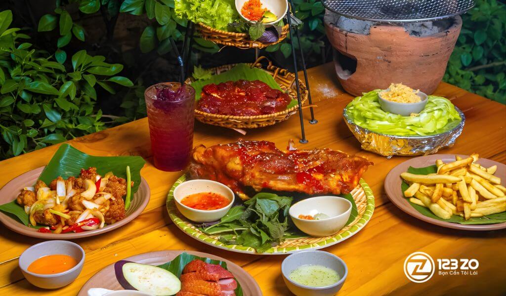 Bàn tiệc ngoài trời tại Tiệm Nướng NỌ với sườn nướng BBQ lớn, khoai tây chiên, rau củ và các món ăn kèm.