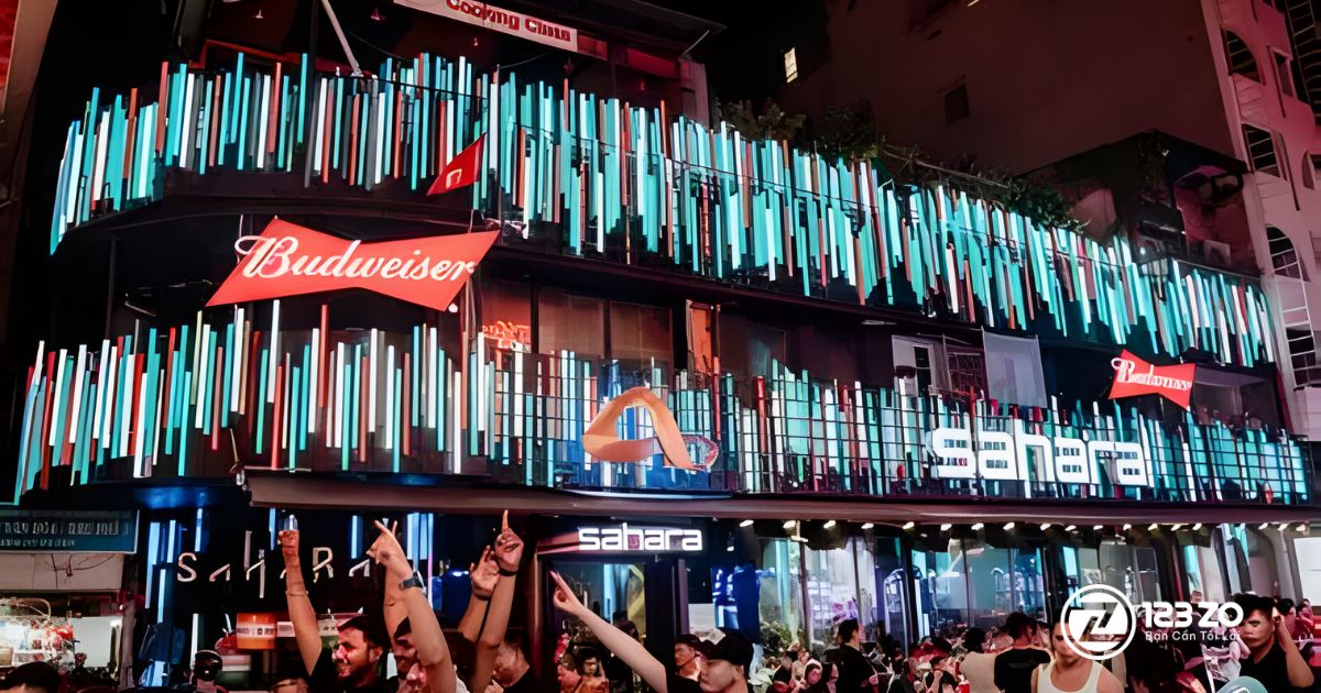 Top 10 quán nhậu, beer club Bùi Viện “hot” nhất Quận 1 2025 8 Quán nhậu, beer club của Sahara Beer Club về đêm, nổi bật với hệ thống đèn LED màu xanh, trắng, và đỏ cùng biển hiệu Budweiser lớn.