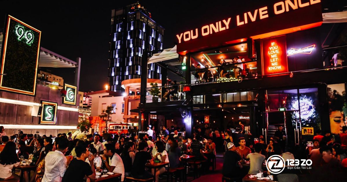 Top 10 quán nhậu, beer club Bùi Viện “hot” nhất Quận 1 2025 11 Quấn nhậu, beer club Yolo Pub & Cafe về đêm, với biển hiệu lớn "YOU ONLY LIVE ONCE" (YOLO) màu đỏ, khu vực ngoài trời đông đúc và một tòa nhà cao tầng có kiến trúc hiện đại phía sau.